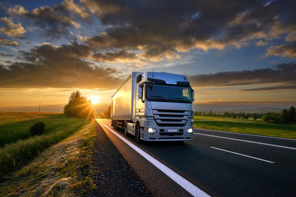 Camion roulant sur la route en asphalte dans un paysage rural au coucher du soleil avec des nuages sombres.